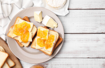 Tasty sandwiches with brie cheese and apricot jam on white wooden table, flat lay. Space for text