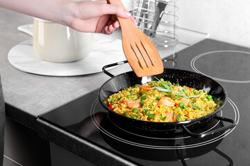 Woman cooking tasty rice with shrimps and vegetables on induction cooktop, closeup