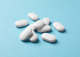 Many white pills on light blue background, closeup