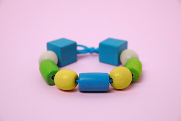 Wooden pieces and string for threading activity on pink background, closeup. Educational toy for...