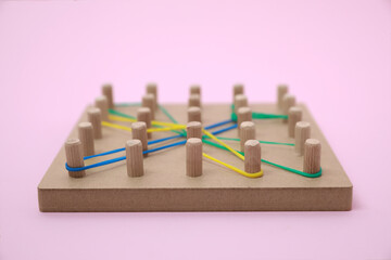 Wooden geoboard with dragonfly shape made of rubber bands on pink background, closeup. Educational...