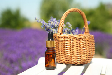 Fototapeta na wymiar Bottle of essential oil and wicker bag with lavender flowers on white wooden surface outdoors, closeup