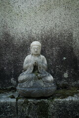 Stone Statue of Buddha in praying position with green moss, Japan   
