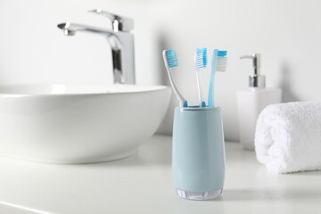 Holder with plastic toothbrushes on white countertop in bathroom, space for text