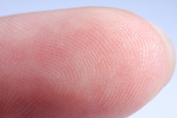 Finger with friction ridges on light blue background, macro view