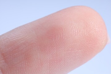 Fototapeta premium Finger with friction ridges on light blue background, macro view