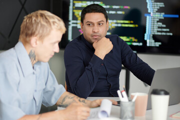 Pensive project manager listening to developer explaining new features he added to the code