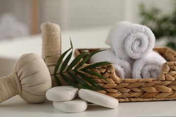Spa composition. Towels, stones, herbal bags and palm leaves on white table indoors, closeup