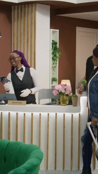 Vertical video Tourists registering at front desk, arriving at vacation resort and doing check in. Woman receptionist welcoming people at hotel, ensuring pleasant stay and fash registration procedure.