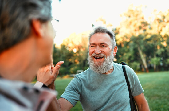 Portrait of attractive bright modern stylish cheerful sporty healthy older man with gray hair and beard giving high five to his partner. A good team, morning training, jogging in the fresh air.