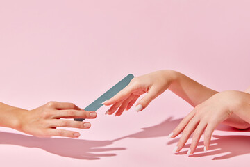 Female hand with nail file taking care after hands, nails against pink background. Elegant natural...