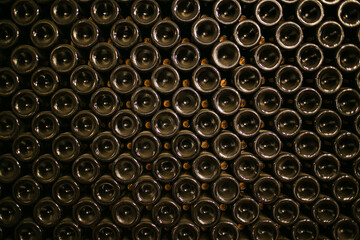 A stack of wine bottles in a wine cellar. The bottles are of different shapes and sizes, all...
