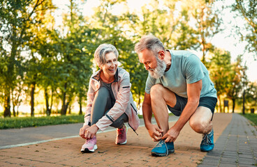 Active pension life. Motivated elderly woman and man making stop for few seconds for tying laces on...
