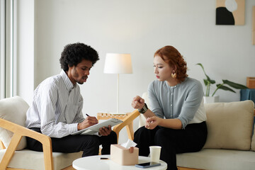 Psychotherapist asking questions and filling form on clipboard when talking to patient