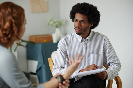 Serious Psychotherapist Listening To Woman Talking About Her Problems And Taking Notes