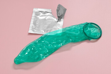 Unrolled condom and torn package on pink background. Safe sex