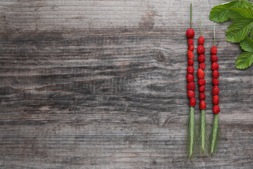 Grass stems with wild strawberries and leaves on wooden table, flat lay. Space for text