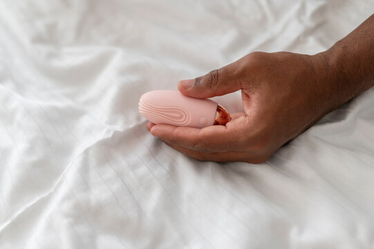 Hand of a young African man holding a pink vibrator,  on a white sheet in a bed