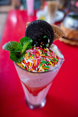 Strawberry milkshake with rainbow sprinkle, cookies, and mint topping. Selective focus, shallow depth of field.