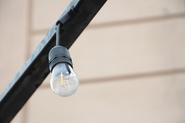 small exterior outdoor string light bulb with black base hanging upside down mounted to metal bar...