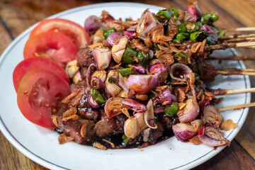Close up goat satay (Sate Kambing) served with tomatoes, shallots, green chili and sweet soy sauce, on a round white plate. Traditional cuisine of Indonesia.