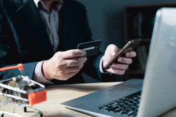 businessman uses a computer laptop and credit card to buy or purchase produce payment online and sits on the chair in the living room at home. The concept of finance and online shopping.