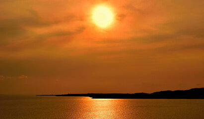 Obraz premium Beautiful sunset over the sea. Sun falling down behind the dark land. Red, orange and yellow color sky and clouds.