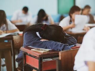 Tired girl student sleeping in a exam test in classroom with stress