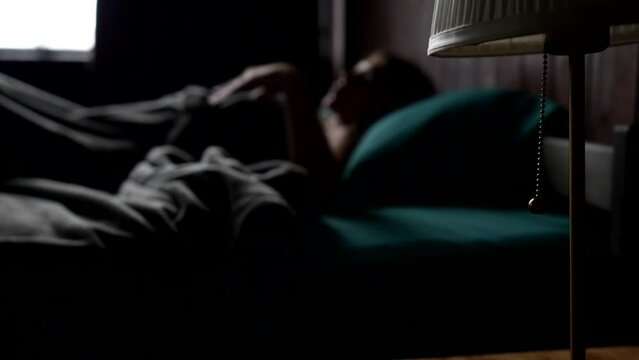 young adult woman sleeping in bed in morning, unfocused blurred shot, focus on table lamp, cinematic shot