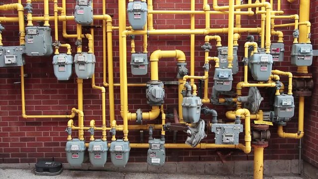 a lot bunch of gray enbridge gas meters bunched together mounted to brick wall with yellow gas pipes coming out of them
