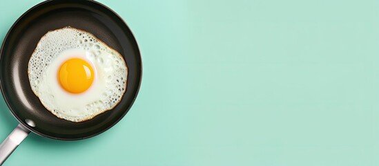 Fried egg sizzling on a black pan isolated pastel background Copy space - obrazy, fototapety, plakaty