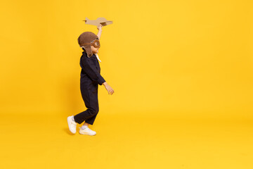 Side view of Asian little boy aviator running and playing with cardboard airplane isolated on yellow background