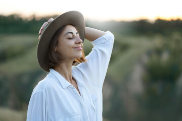 Graceful young lady in hat enjoying the beauty of nature amidst serene hillside landscapes during a captivating sunset