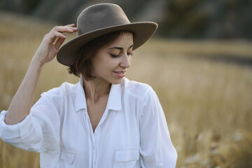 Portrait of beautiful stylish woman in hat posing in field with dry yellow grass.