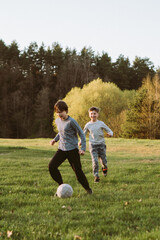 Happy boy running behind concentrated teenager who dribbling ball in game of football, friends playing soccer on field.