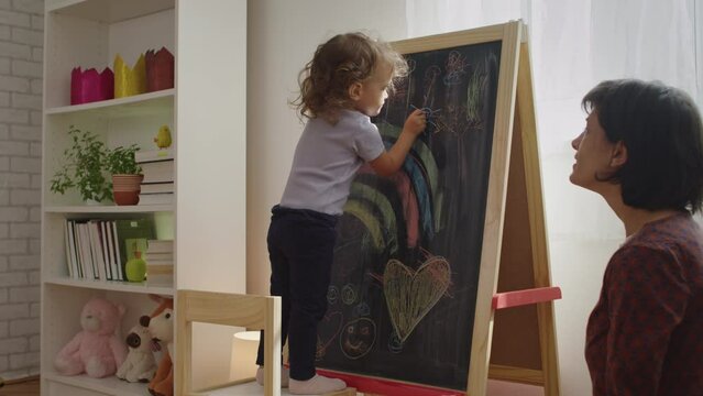 Mother and child drawing together on chalk board at home. 