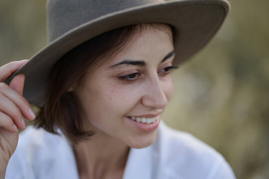 Close up face of beautiful young woman in hat at lawn with dry yellow grass