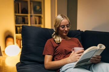 Pretty woman reading a book in the evening in the living room.