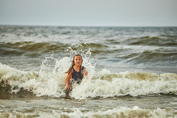 Little girl playing with waves in the sea. Kid playfully splashing in waves. Child jumping in sea. Vacations on the beach. Water splashes