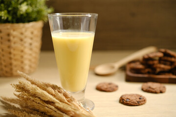 Tasty fresh corn milk in glass and cobs on white wooden table