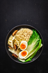 Gyoza ramen - broth with traditional Japanese dumplings filled with vegetables wrapped into thin dough, noodles boiled eggs and vegetables on wooden table
