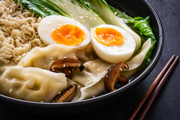 Gyoza ramen - broth with traditional Japanese dumplings filled with vegetables wrapped into thin dough, noodles boiled eggs and vegetables on wooden table
