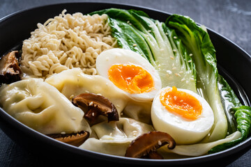 Gyoza ramen - broth with traditional Japanese dumplings filled with vegetables wrapped into thin dough, noodles boiled eggs and vegetables on wooden table
