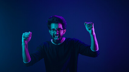 Happy Indian man in ultraviolet neon studio background champion coding achievement level up...