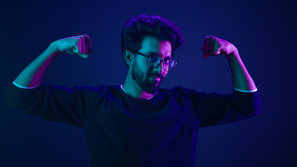 Proud slim weak Arabian man coder guy technology hacker show hands muscle bicep sport strong power like bodybuilder neon studio background champion boast efficient security coding achievement level up