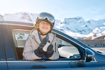 Joyful boy riding in car against snowy mountains