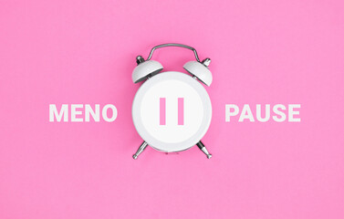 White vintage alarm clock with an inscription MENOPAUSE on pink background.