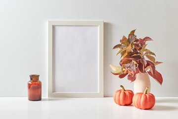 Mockup with a white frame and colorful autumn leaves in a vase on a light background. Empty poster...