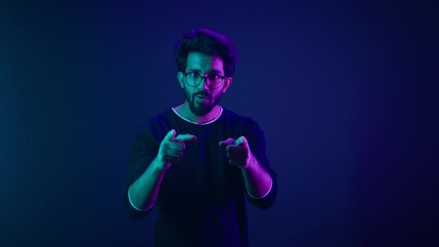 Neon ultraviolet background happy Indian guy Arabian man worker coder hacker computer engineer showing hey gesture pointing at camera smiling satisfied show thumbs up support good idea agree recommend