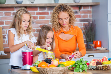 Mother and daughters cooking together in the kitchen. Healthy food concept. Portrait of happy family with fresh smoothies. Happy sisters.